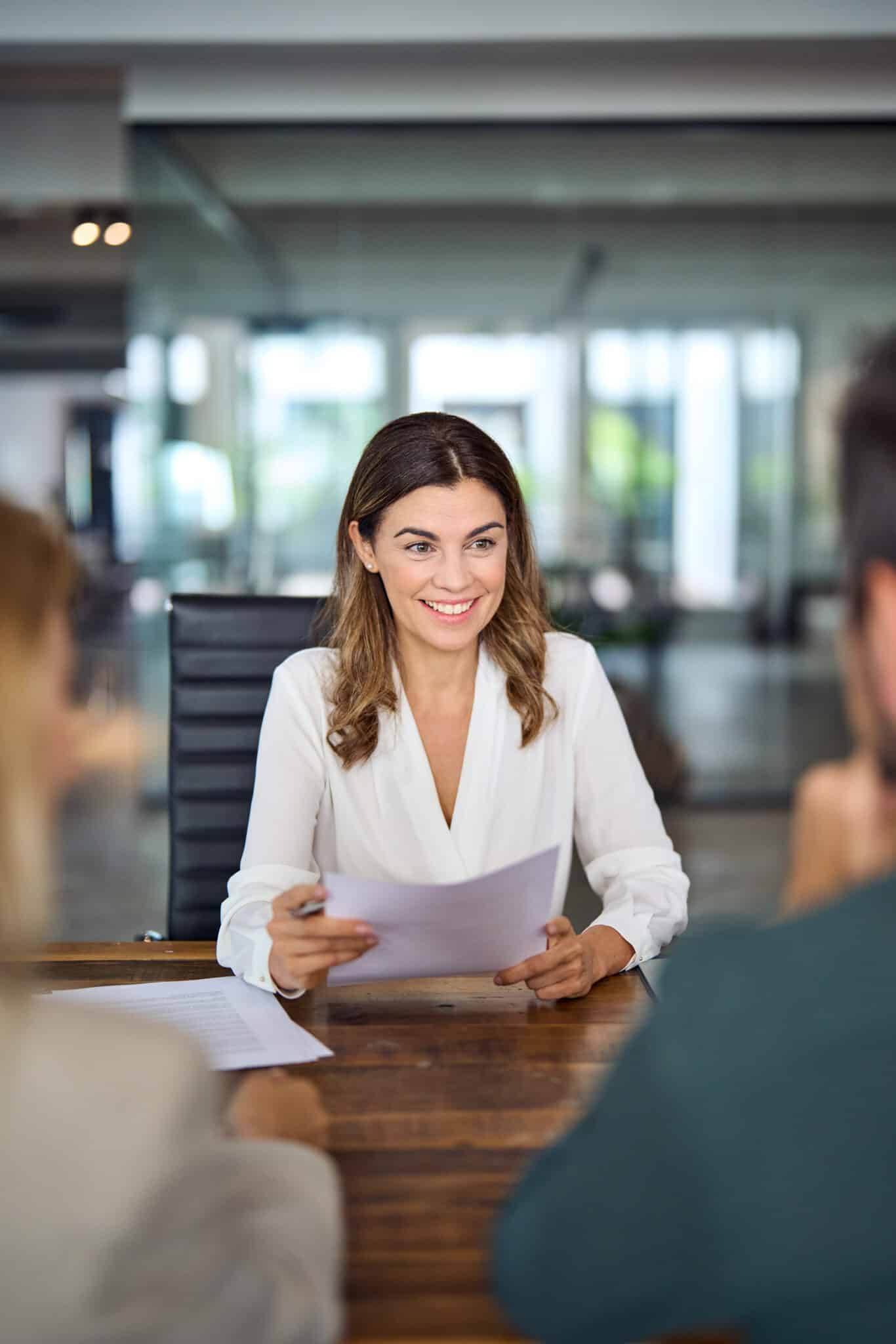 Smiling mature professional business woman banking loan manager, insurance agent, lawyer or financial advisor consulting clients couple sitting at work corporate office meeting. Vertical